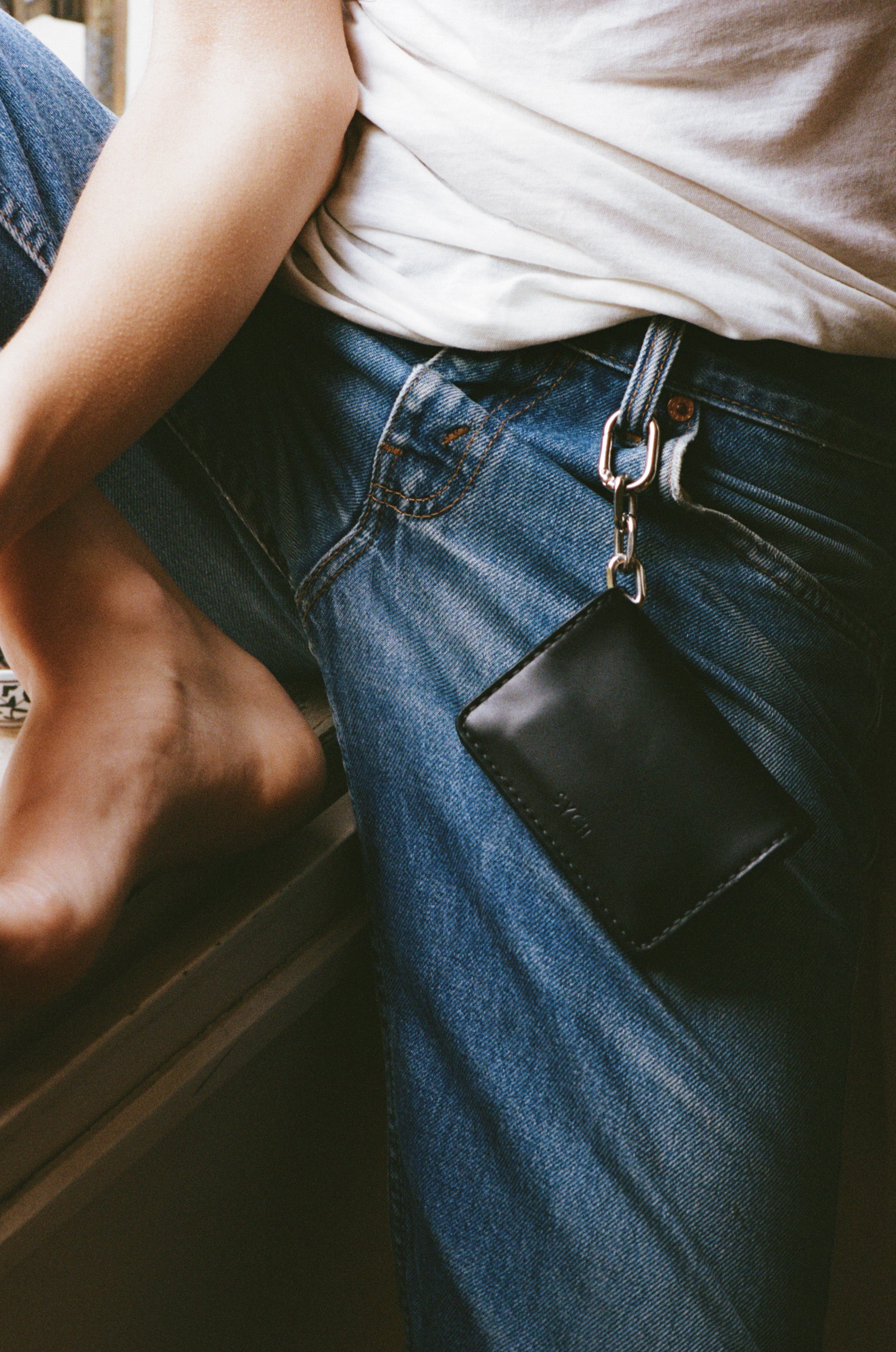 Person wearing blue jeans with a black tobacco pouch attached to the belt loop.