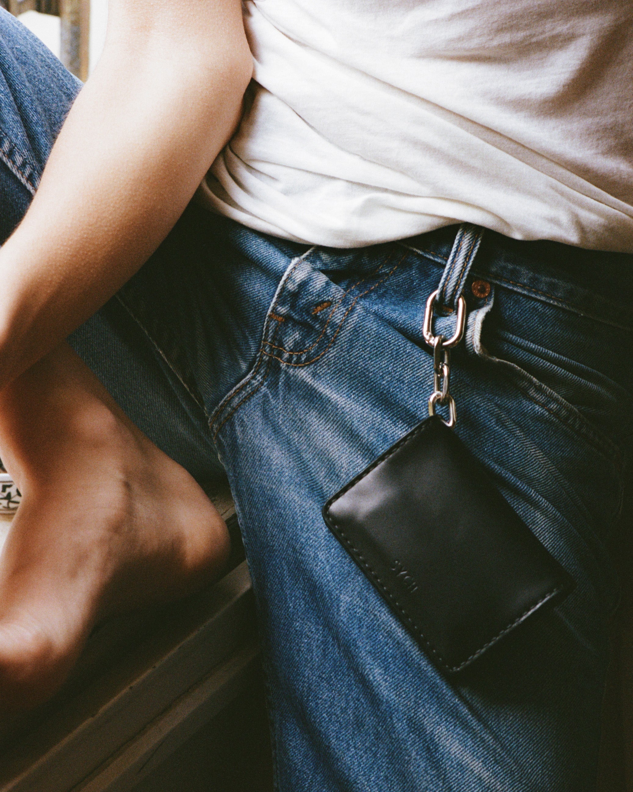 Person wearing blue jeans with a black tobacco pouch attached to the belt loop.