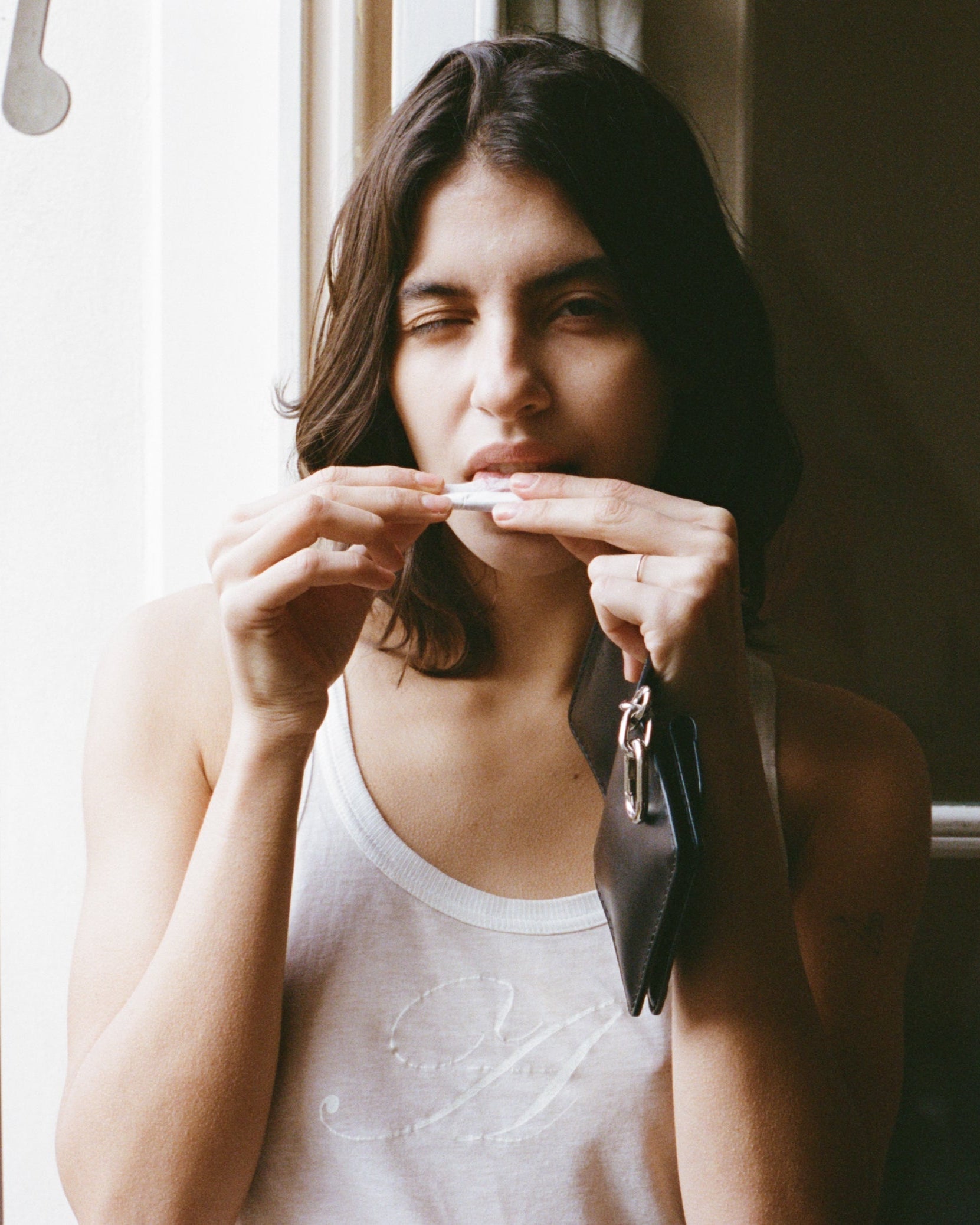 Woman holding a tobacco pouch near her mouth by a window