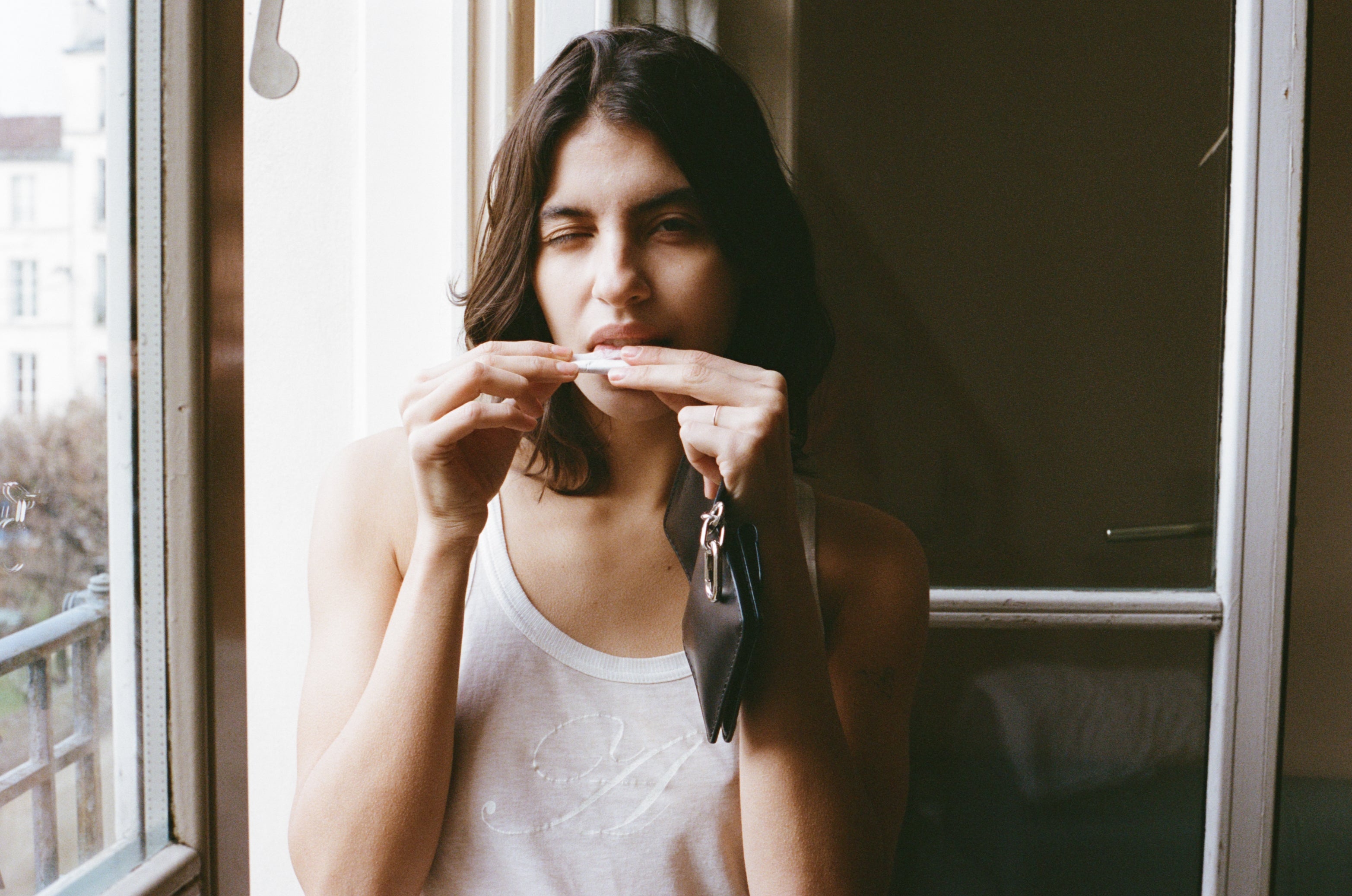 Woman holding a tobacco pouch near her mouth by a window

